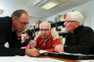 Claude, Jean-Claude et Bertrand s'entraident déchiffrer un document d'état civil rédigé en vieux Français © Charles Crié/CCAS